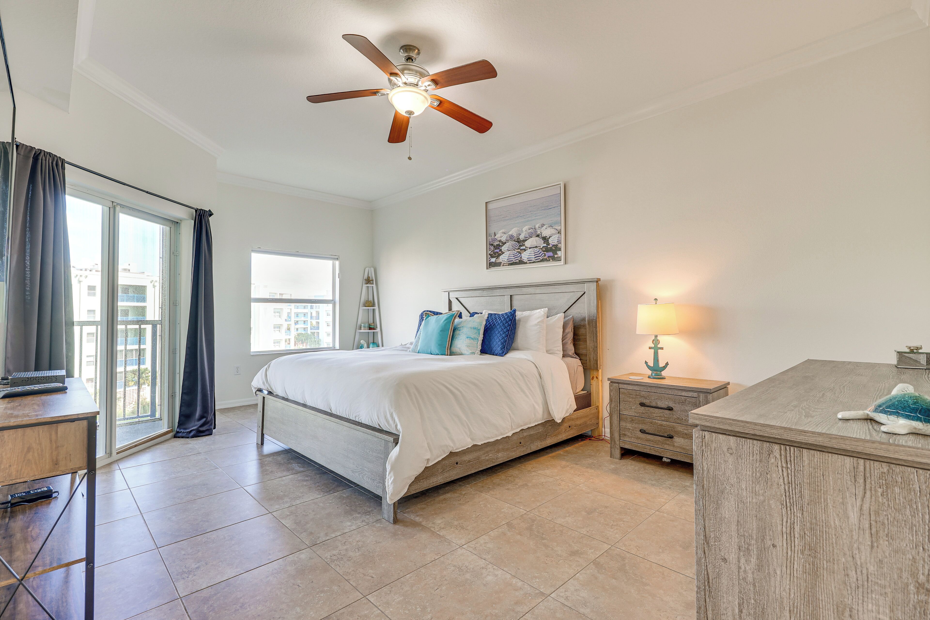 A bedroom with a bed, a desk, a nightstand, a ceiling fan, a window, and a lamp.