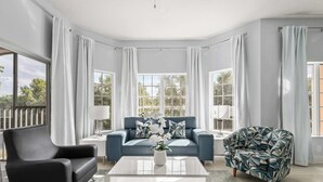 Una sala moderna con un sofá de cuero negro, un sillón estampado y una mesa de centro blanca.