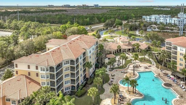 Un hotel de varios pisos con piscina, rodeado de palmeras y una vista despejada del paisaje circundante.