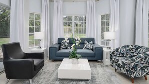 Un salon moderne avec un canapé foncé, un fauteuil à motifs et une table basse blanche agrémentée d’une plante.
