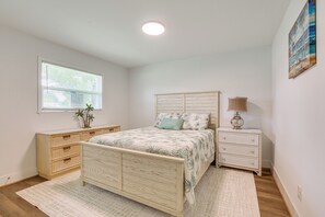 A bedroom with a wooden bed, a bedside table with a lamp, a dresser, and a window with blinds. - 2 Mi to River District! Fort Myers Retreat w/ Yard (Fort Myers)