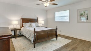 A bedroom with a wooden bed, two bedside tables, a ceiling fan, a window, and a framed picture on the wall. - 2 Mi to River District! Fort Myers Retreat w/ Yard (Fort Myers)