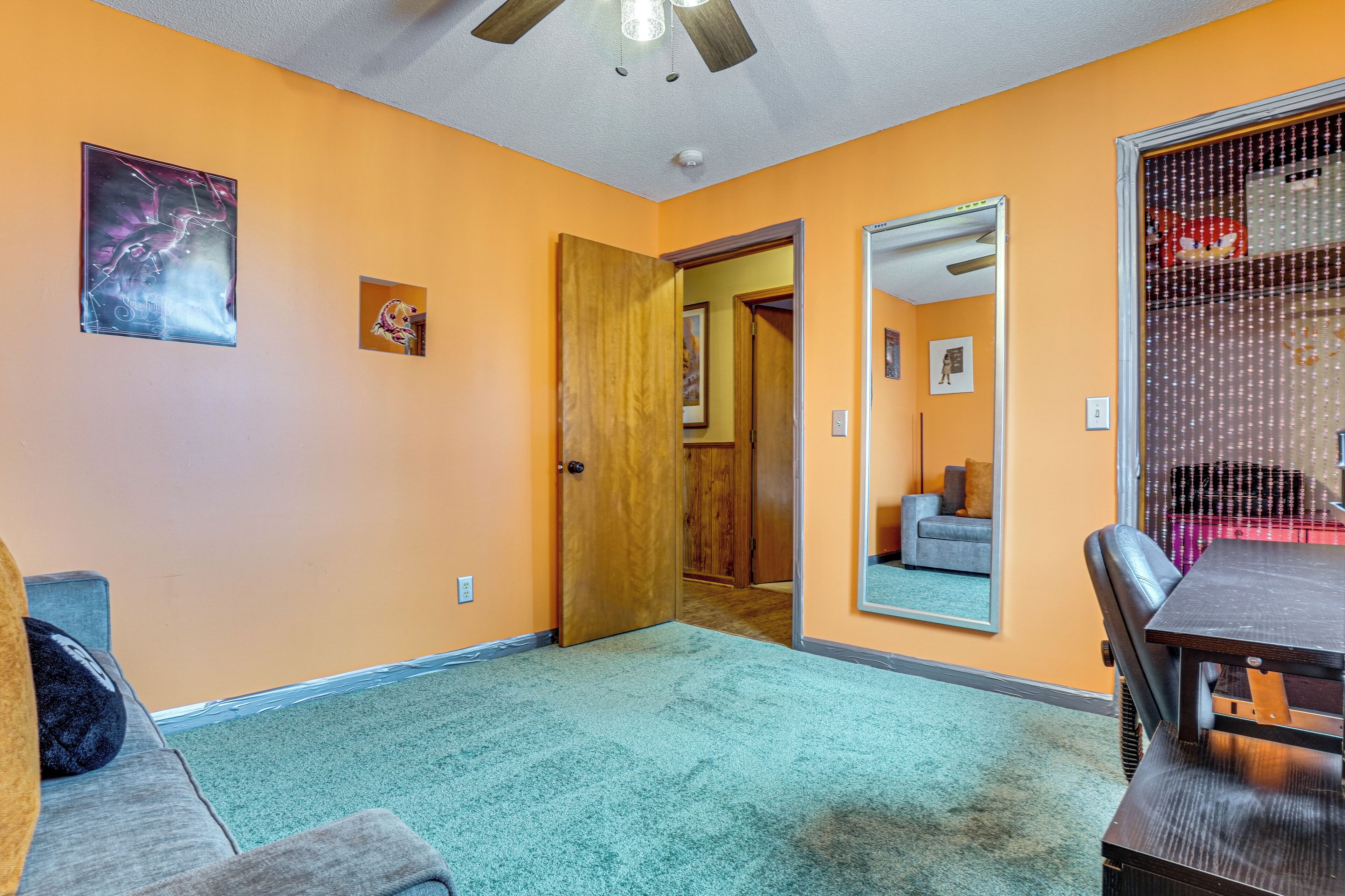 A room with orange walls, a wooden door, a gray sofa, a dining table, and a mirror.