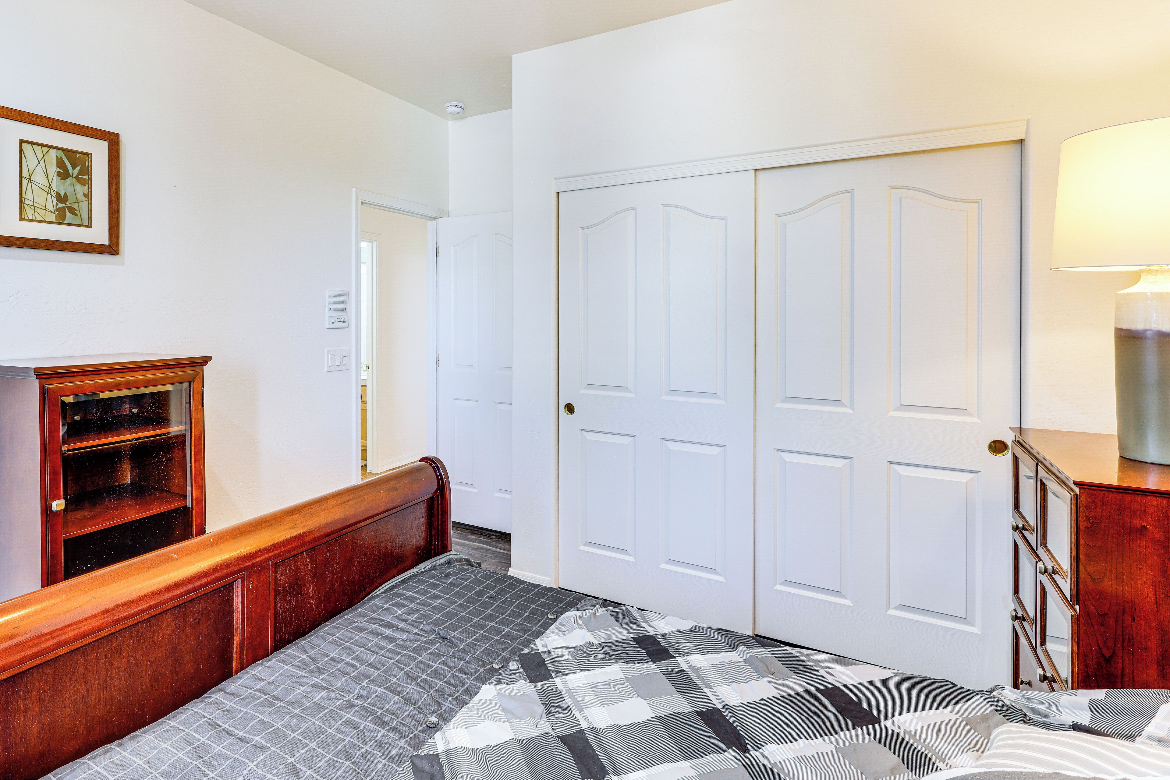A bedroom with a bed, a wooden dresser, a white wardrobe, and a framed picture on the wall.