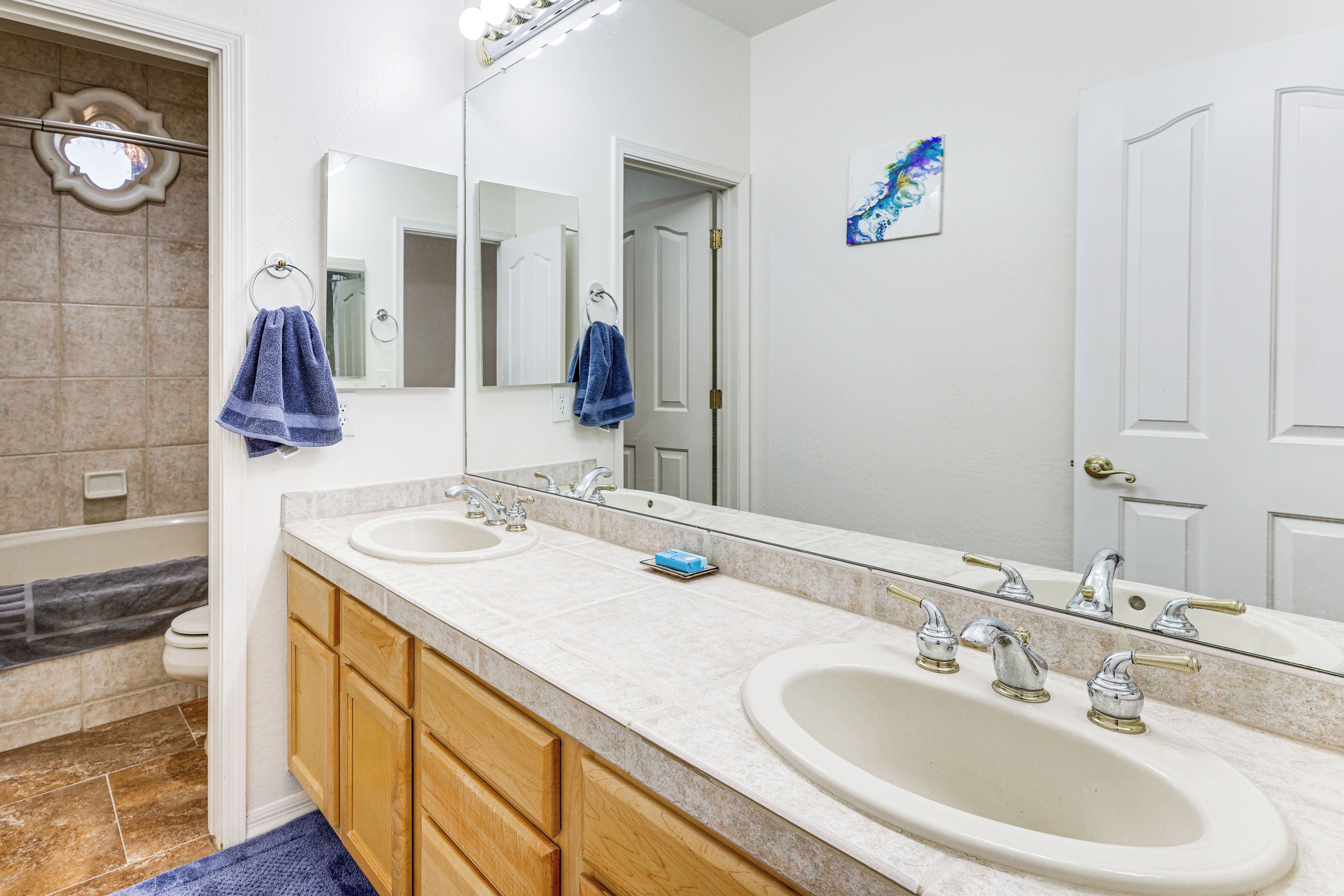 A bathroom with two sinks, a large mirror, wooden cabinets, and a towel rack.