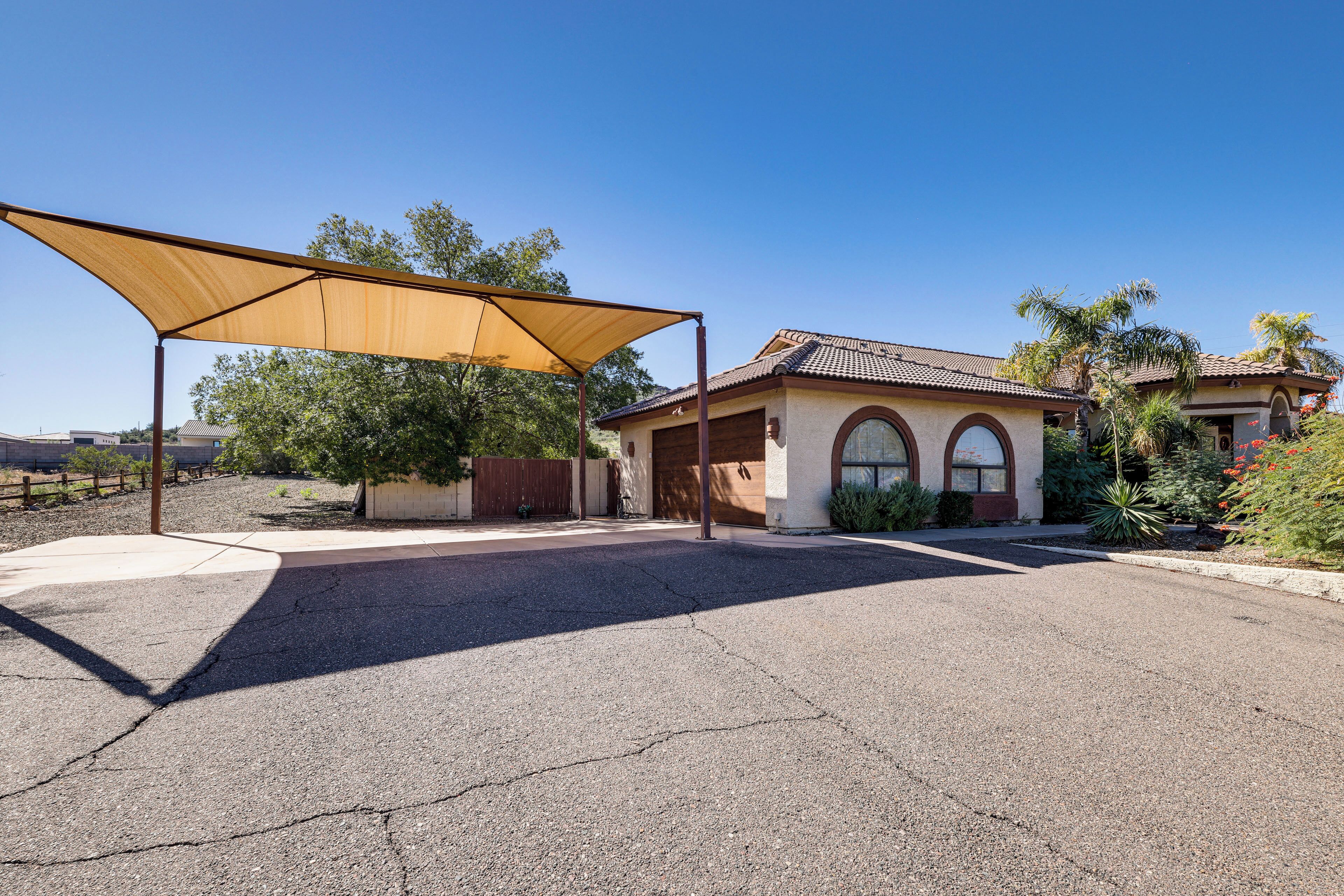 A residential property with a covered driveway, a house with a tiled roof, and a palm tree in the yard.