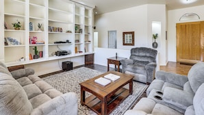 A living room with a sectional sofa, a coffee table, a bookshelf, and a grey armchair. - Groups Welcome! Home w/ Pool + Patio in N Phoenix (Phoenix)