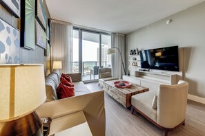 A modern living room with a sofa, armchair, coffee table, and a flat-screen TV. - Luxe Condo w/ Hallandale Beach Oceanfront View! (Hollywood)