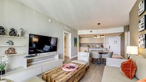 A modern living room with a flat-screen TV, a wooden coffee table, and a sofa with a cushion. - Luxe Condo w/ Hallandale Beach Oceanfront View! (Hollywood)