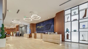 A modern reception area with a wooden reception desk, a large wall mural, and a display of decorative items. - Luxe Condo w/ Hallandale Beach Oceanfront View! (Hollywood)