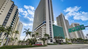 A high-rise building with multiple floors, surrounded by palm trees and other tall buildings. - Luxe Condo w/ Hallandale Beach Oceanfront View! (Hollywood)