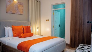 A neatly made bed with white and orange bedding, a wooden headboard, and a wall-mounted abstract painting. - BLUEBERRY VILLAS (Eldoret)