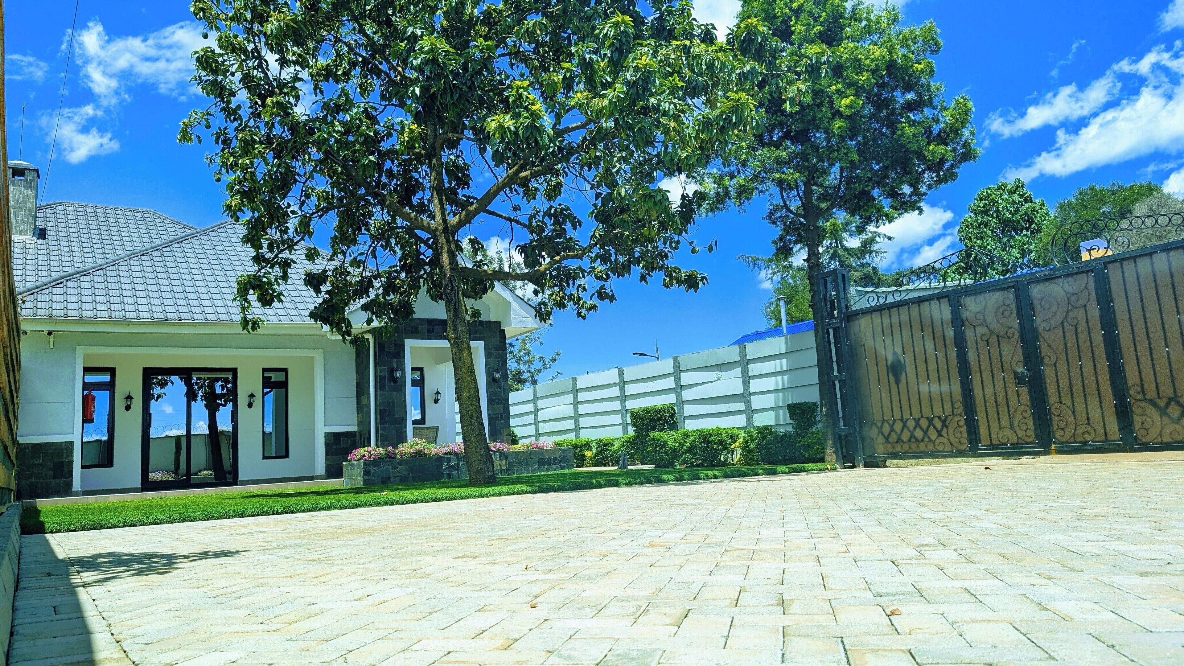A spacious courtyard with a paved walkway, a white building with a glass door, and a metal gate.