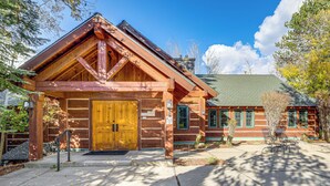A log cabin-style building with a prominent wooden entrance, a stone chimney, and a patio area with outdoor seating. - 2 Mi to Payette Lake: Charming Cottage w/ Hot Tub! (McCall)