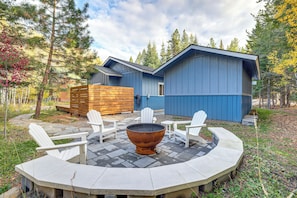 A modern outdoor seating area with Adirondack chairs and a fire pit, surrounded by a stone patio and a wooden deck.