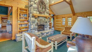 A cozy log cabin interior with a stone fireplace, wooden bookshelves, and comfortable seating. - 2 Mi to Payette Lake: Charming Cottage w/ Hot Tub! (McCall)
