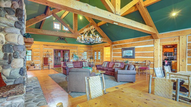 A spacious log cabin interior with a large wooden dining table, multiple sofas, and a stone fireplace. - 2 Mi to Payette Lake: Charming Cottage w/ Hot Tub! (McCall)