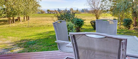 Un patio con dos sillas mirando hacia un campo cubierto de césped y árboles, con una montaña al fondo.