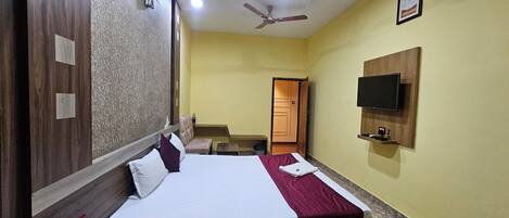A hotel room with a bed, a television mounted on the wall, a ceiling fan, and a door leading to another room.
