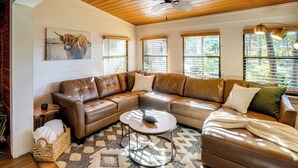 A cozy living room with a brown leather sectional sofa, a round coffee table, and a patterned rug. - Lake Okeechobee Dockside Cabin w/ Pool Access (Okeechobee)