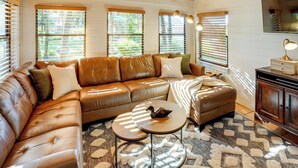 A cozy living room with a brown leather sectional sofa, a small round coffee table, and a patterned rug. - Lake Okeechobee Dockside Cabin w/ Pool Access (Okeechobee)