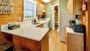A kitchen with wooden cabinets, a white countertop, a stove, and a microwave. - Lake Okeechobee Dockside Cabin w/ Pool Access (Okeechobee)