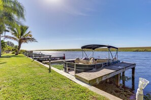 A boat docked at a pier with a grassy area and a palm tree nearby. - Lake Okeechobee Dockside Cabin w/ Pool Access (Okeechobee)