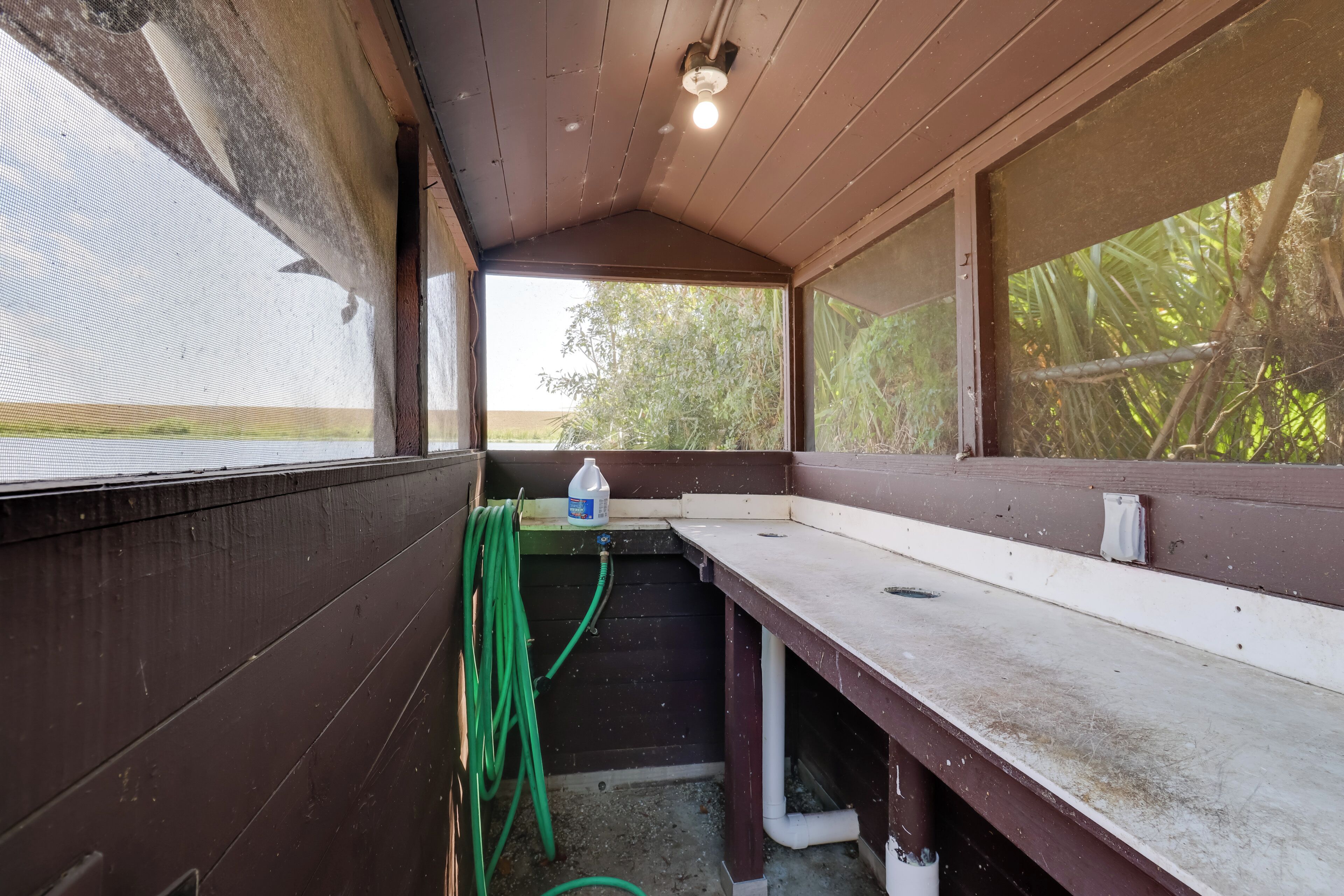 A covered outdoor area with a bench, a hose, and a water container.