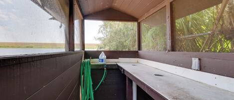A covered outdoor area with a bench, a hose, and a water container.