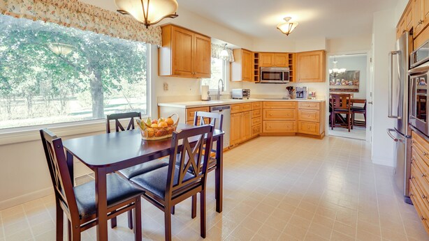A spacious kitchen with wooden cabinets, a dining area with a table and chairs, and a large window providing natural light. - Jackson Home w/ Fire Pit: Near Parks & Downtown! (Jackson)