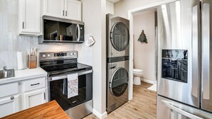 Una cocina moderna con armarios blancos, electrodomésticos de acero inoxidable, encimera de madera y horno empotrado.