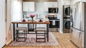Una cocina moderna con armarios blancos, electrodomésticos de acero inoxidable, una mesa de madera con dos taburetes y una alfombra estampada.