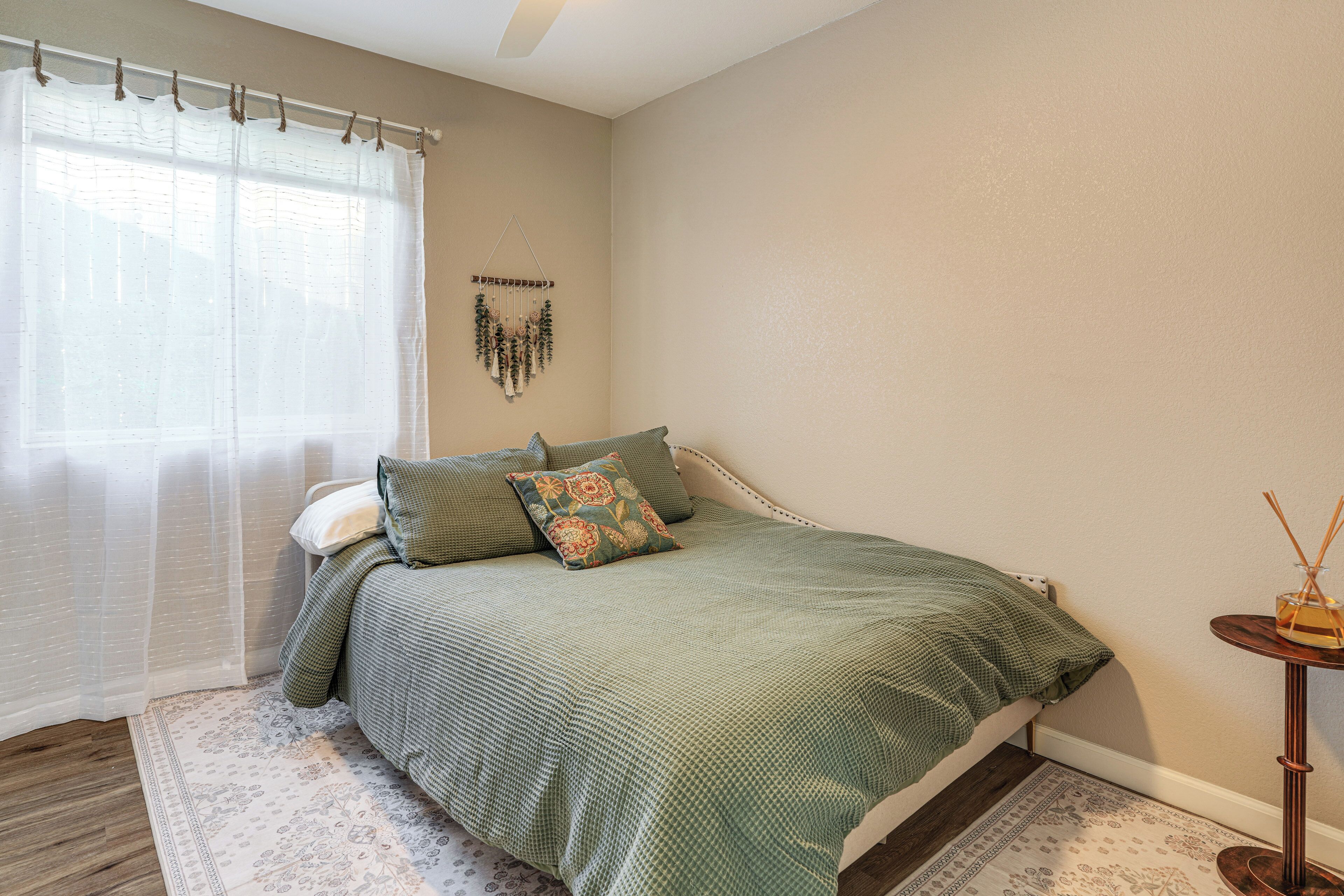 A bedroom with a bed, a bedside table, a wall hanging, and a window with curtains.