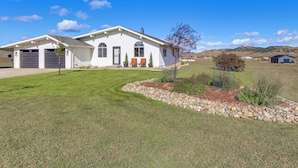 A single-story house with a garage, a small porch with two chairs, and a well-maintained lawn. - Mtn Views, Hot Tub + Fire Pit: Black Hills Retreat (Piedmont)