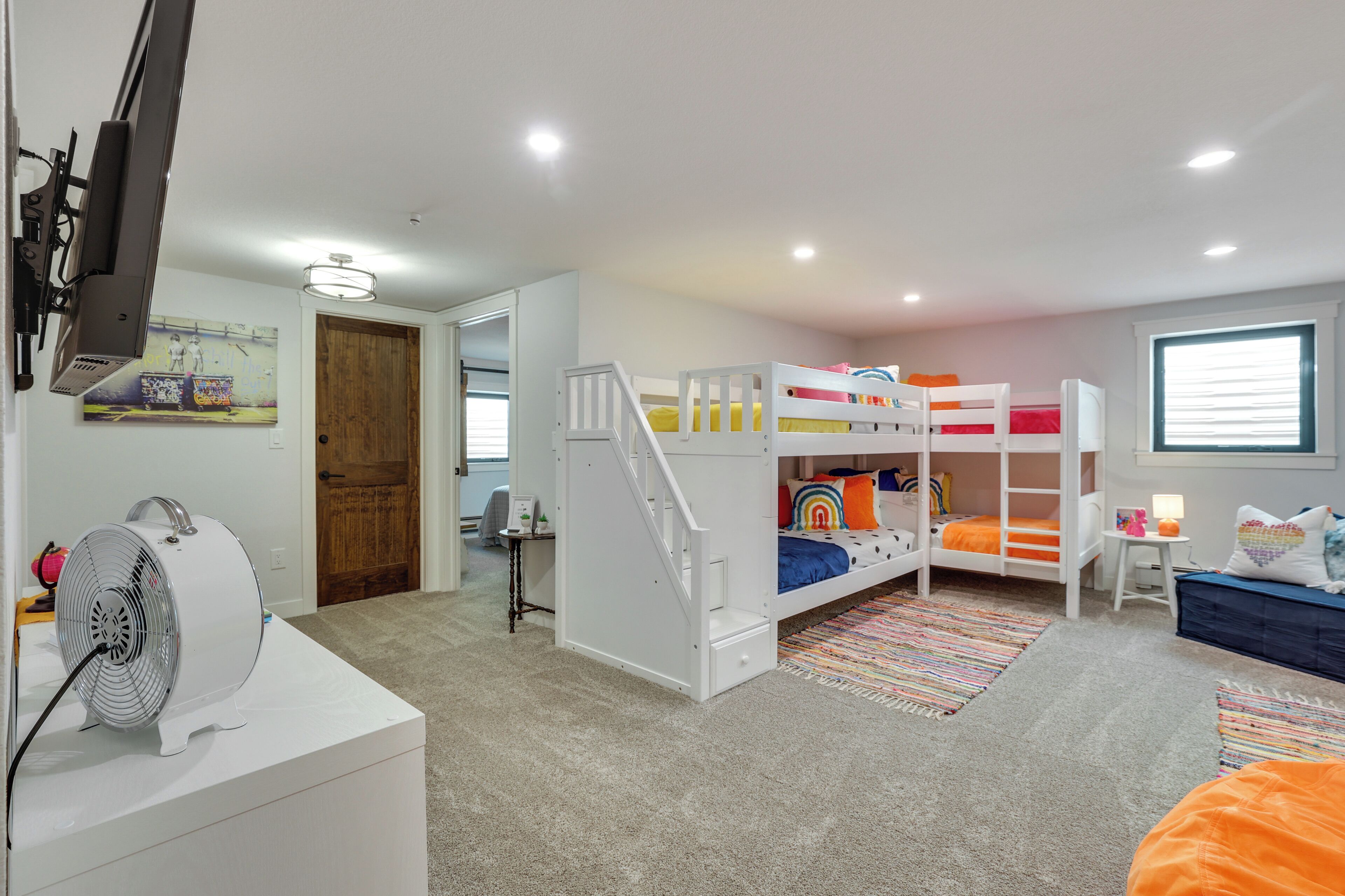 A child's bedroom with bunk beds, a desk, and a fan.