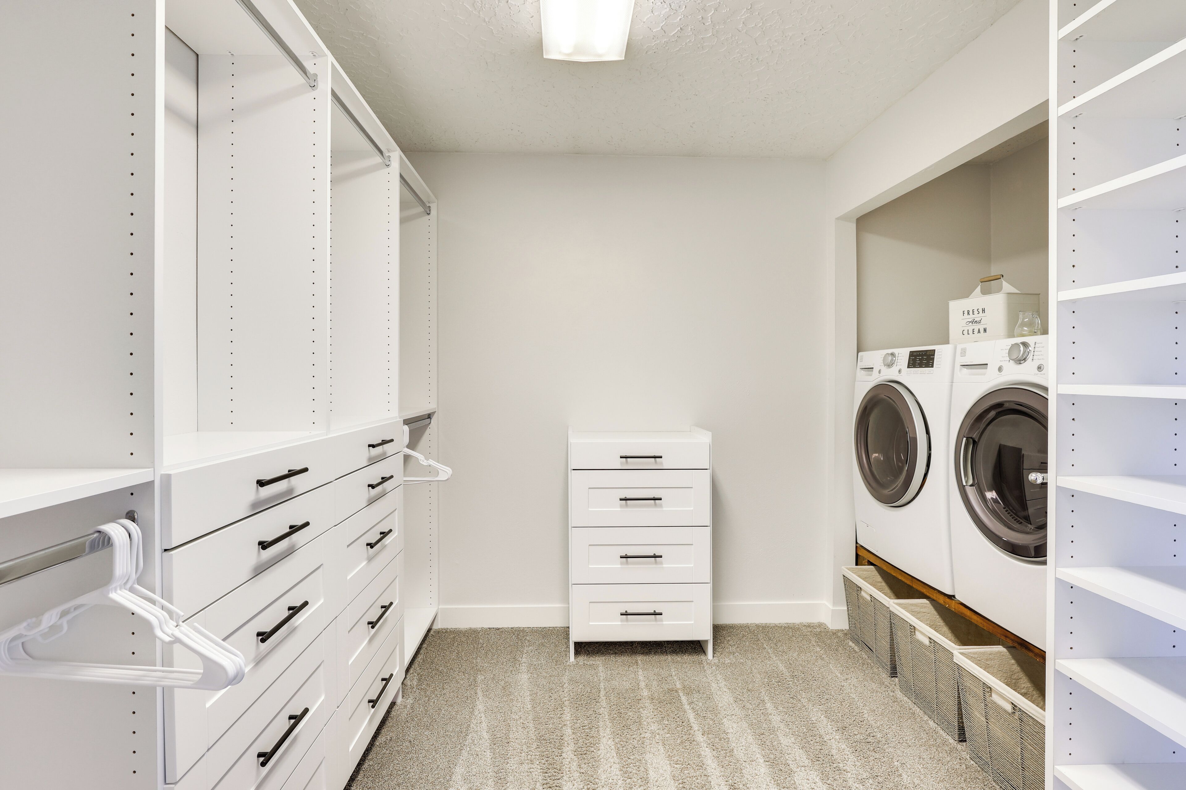 A laundry room with white cabinets, a washer and dryer, and a storage unit with drawers and shelves.