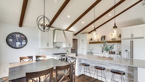 A modern kitchen with wooden beams, a large island with stools, and a wall clock. - Mtn Views, Hot Tub + Fire Pit: Black Hills Retreat (Piedmont)