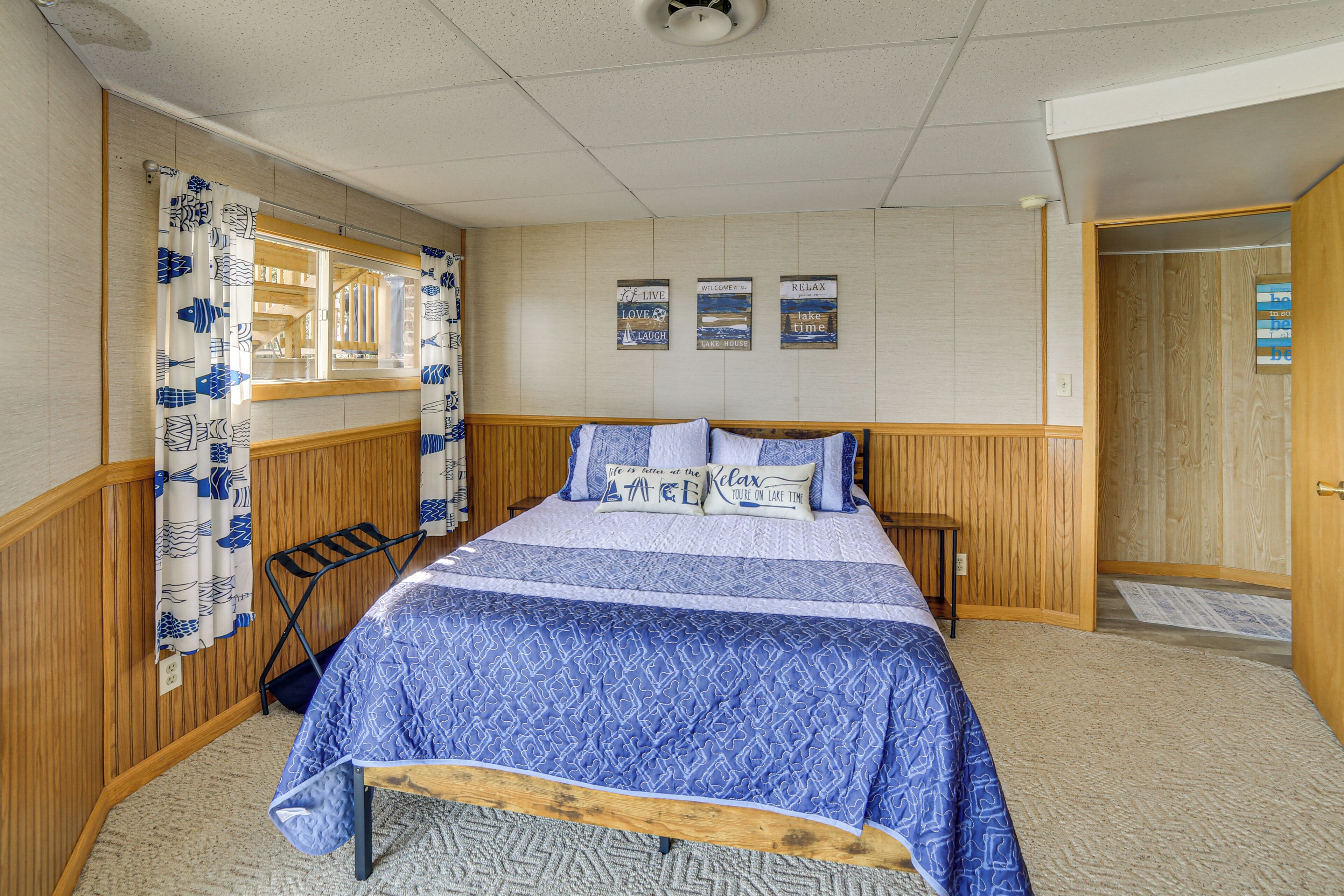 A bedroom with a bed, wooden paneling, a window with curtains, and wall decorations.
