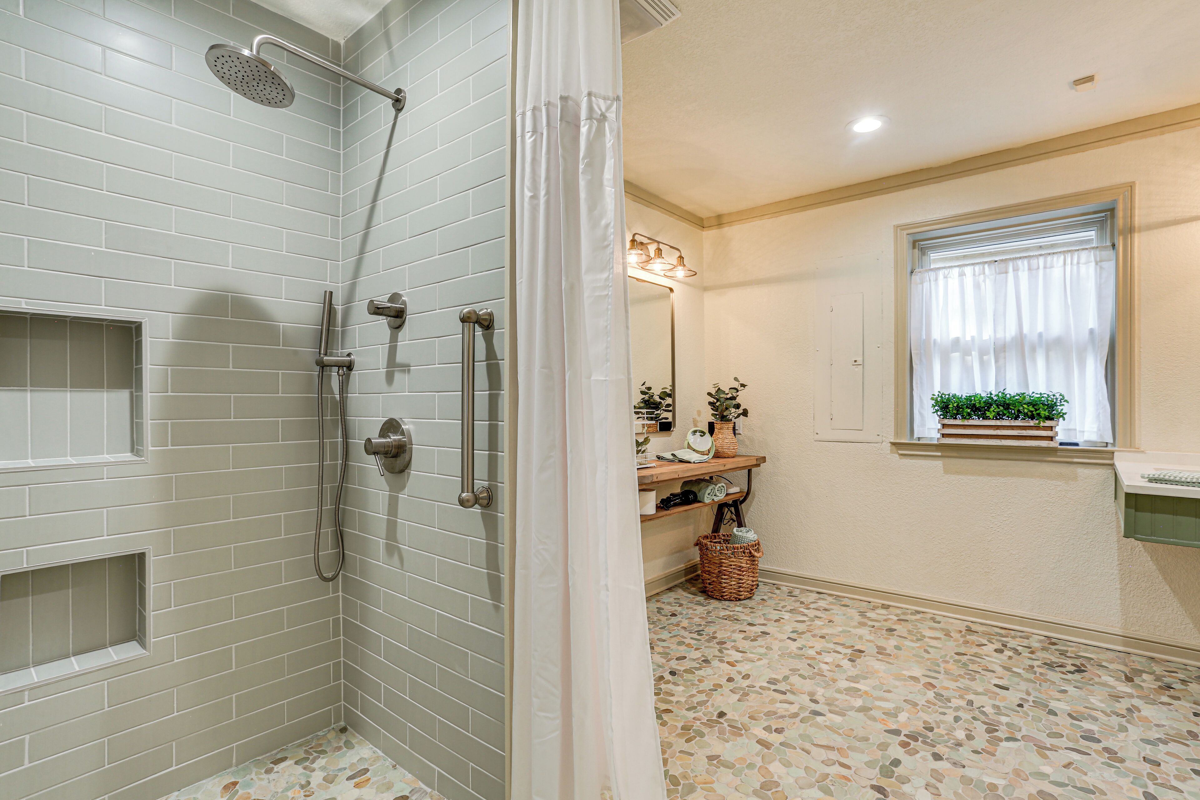 A bathroom with a shower, a sink, a window with a plant, and a tiled floor.