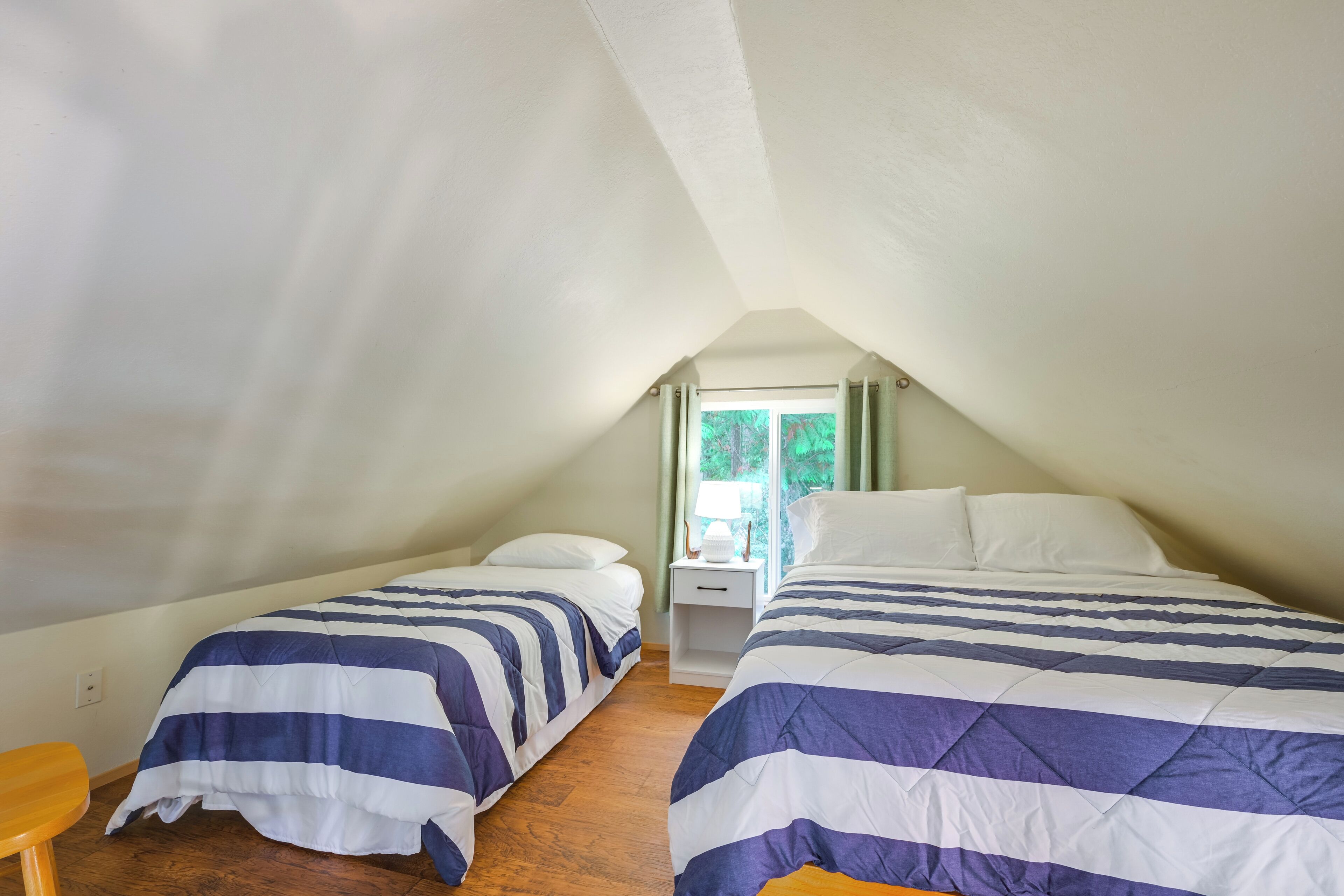 A bedroom with two beds, a wooden floor, a small table, and a window with curtains.