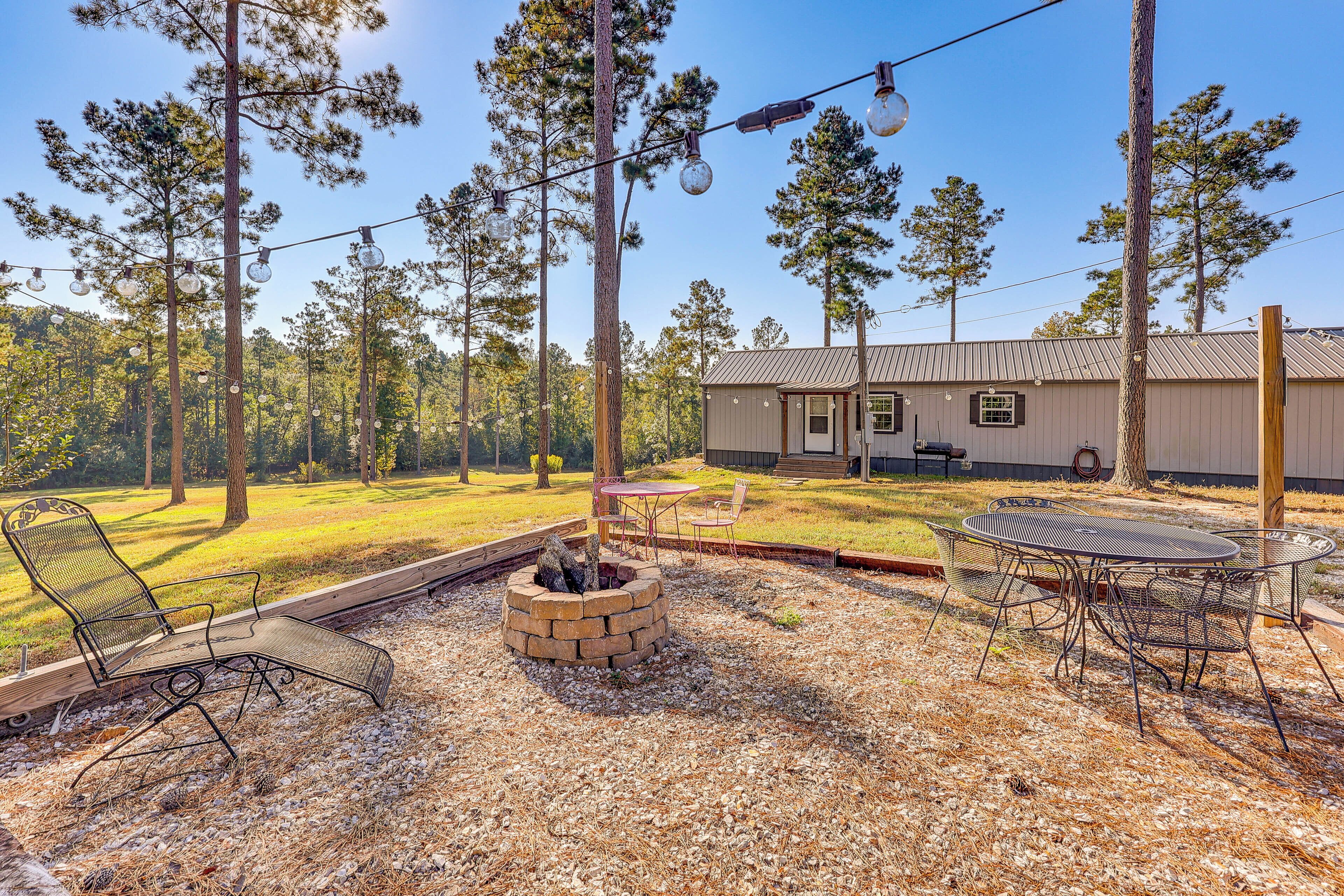 A backyard with a fire pit, outdoor seating, and string lights.