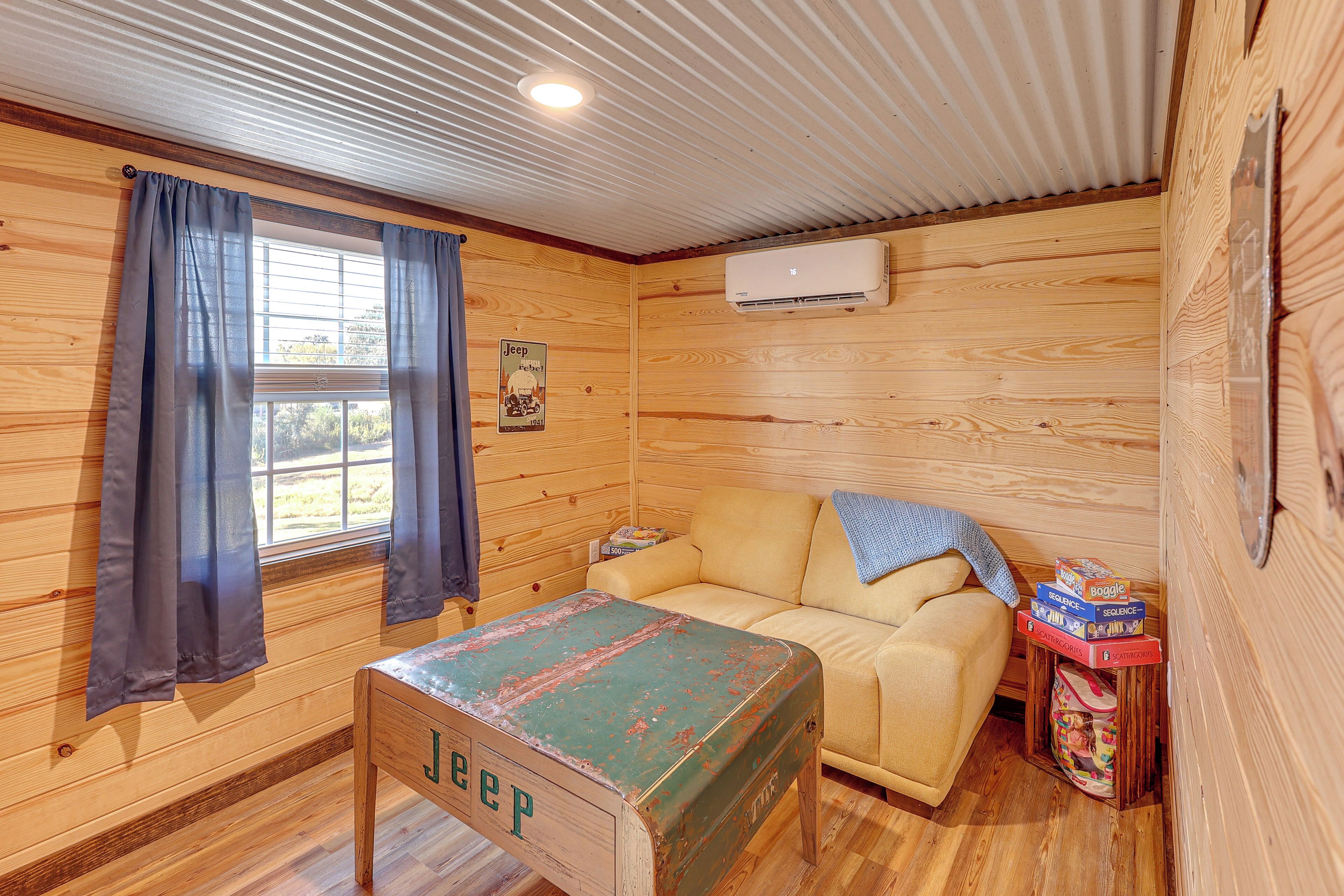 A cozy room with a wooden interior, a beige sofa, a small table with a 'Jeep' sign, and an air conditioning unit on the wall.