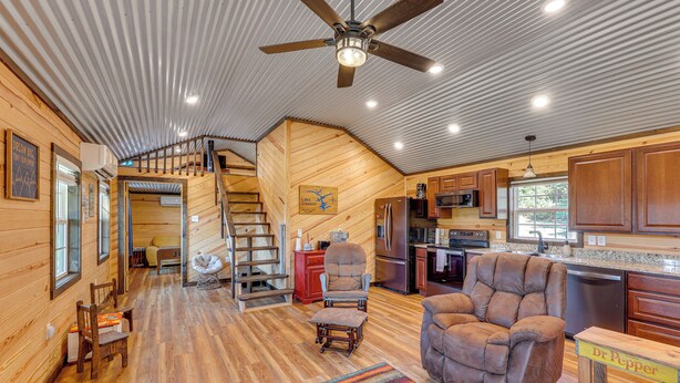A spacious cabin interior with a wooden floor, a large brown leather chair, a dining area, and a kitchen with wooden cabinets. - ~ 1 Mi to Lake Greeson & Ramp: 'lazy Bear Cabin' (Amity)