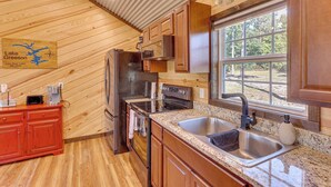 A cabin kitchen with wooden walls, a granite countertop, stainless steel appliances, and a window overlooking a natural landscape. - ~ 1 Mi to Lake Greeson & Ramp: 'lazy Bear Cabin' (Amity)