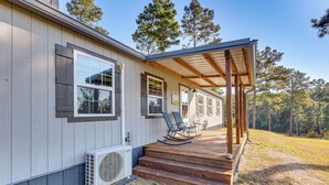 A single-story house with a covered porch, a small outdoor seating area, and a large air conditioning unit. - ~ 1 Mi to Lake Greeson & Ramp: 'lazy Bear Cabin' (Amity)
