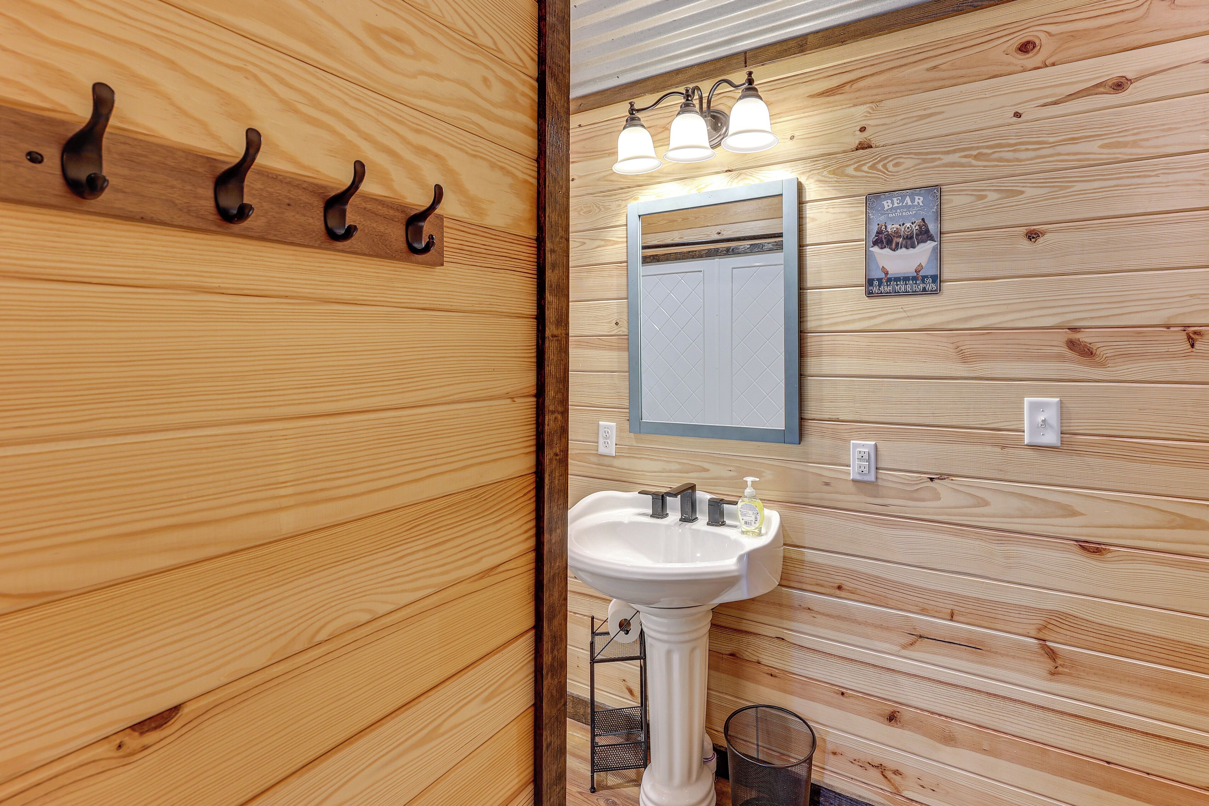 A wooden wall with a white sink, three hooks, a mirror, and a bear-themed poster.