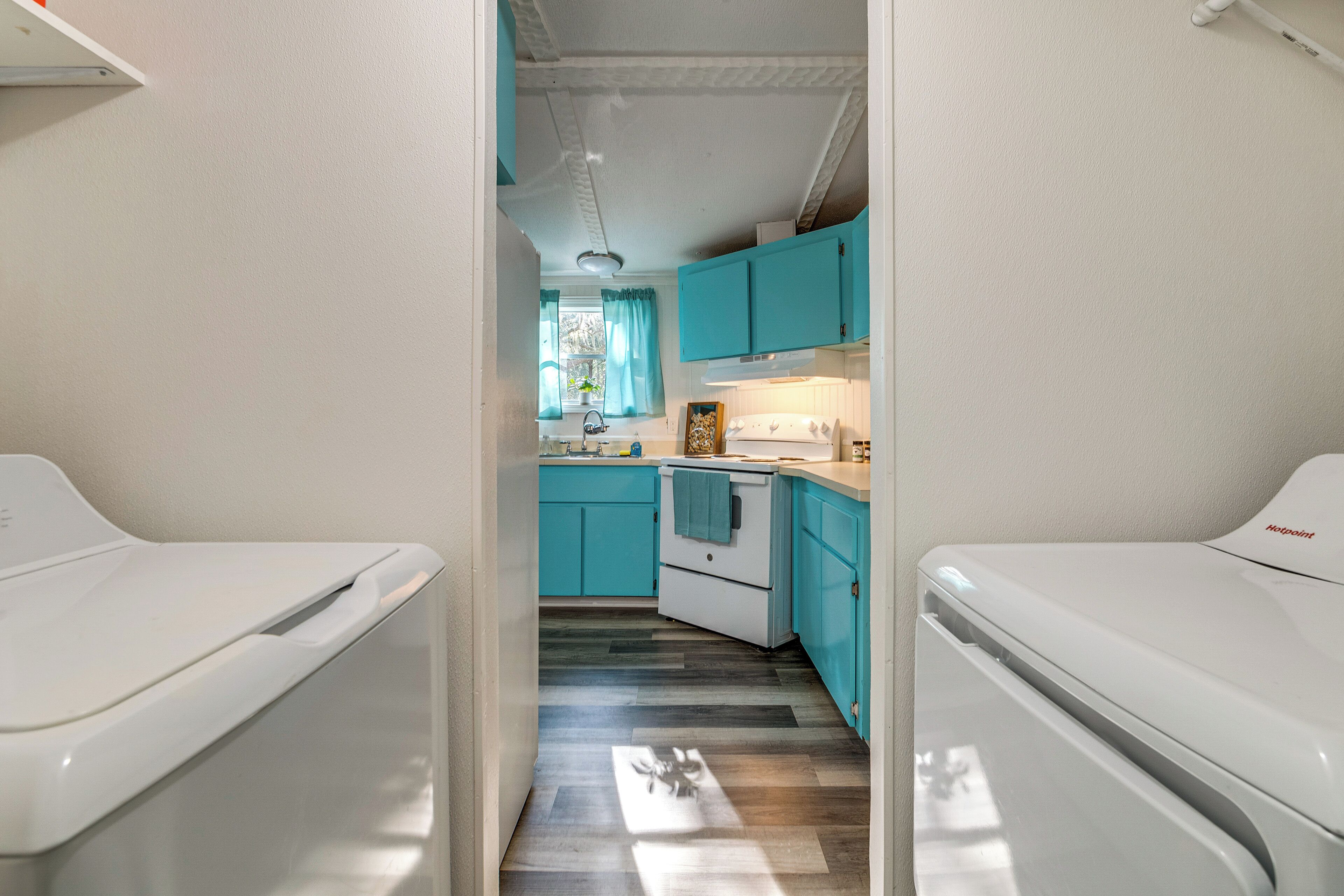 A compact kitchen with teal cabinets, a white stove, and a window with curtains.