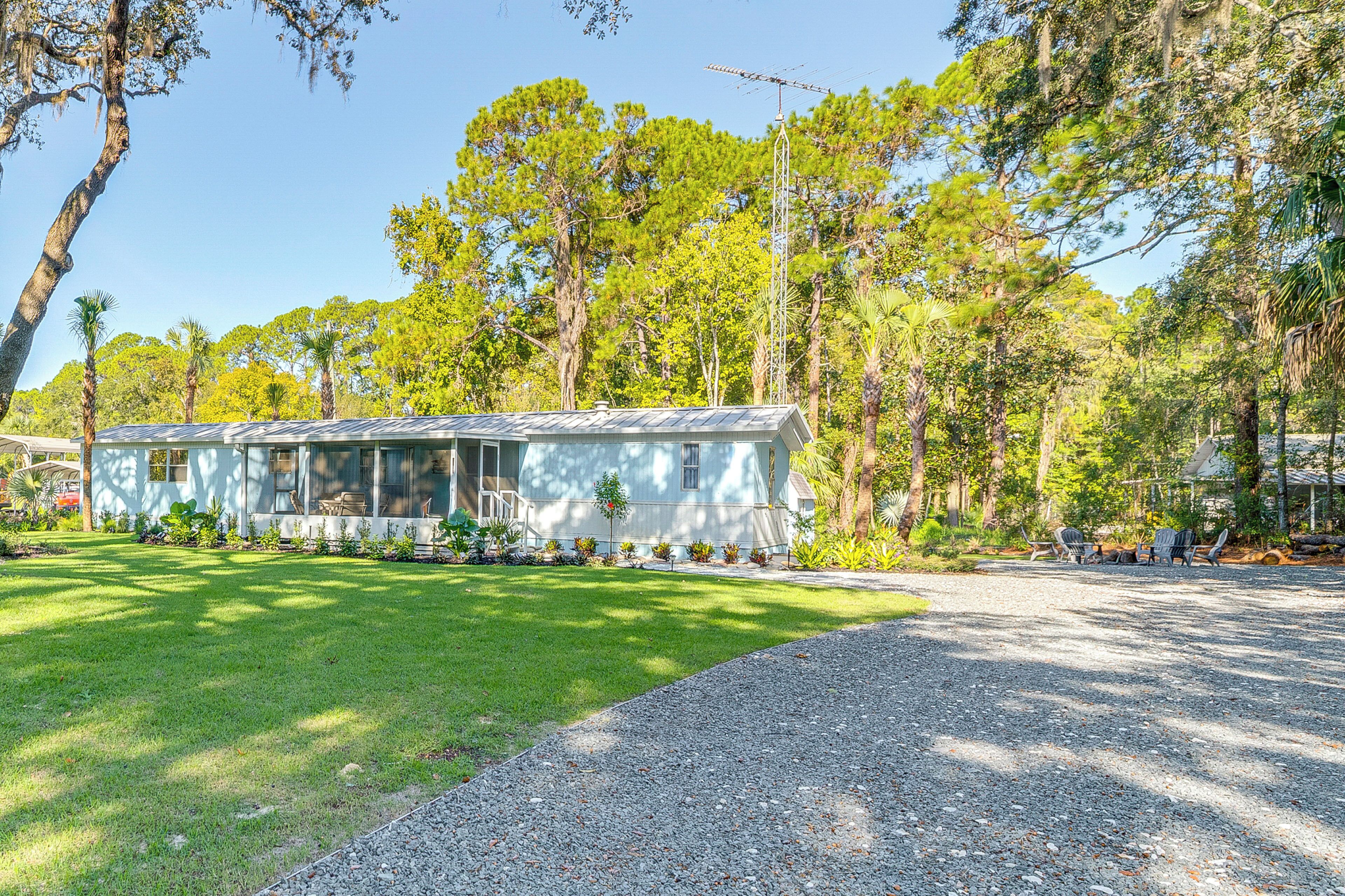 A single-story house with a sloped roof, surrounded by a well-maintained lawn and dense trees.