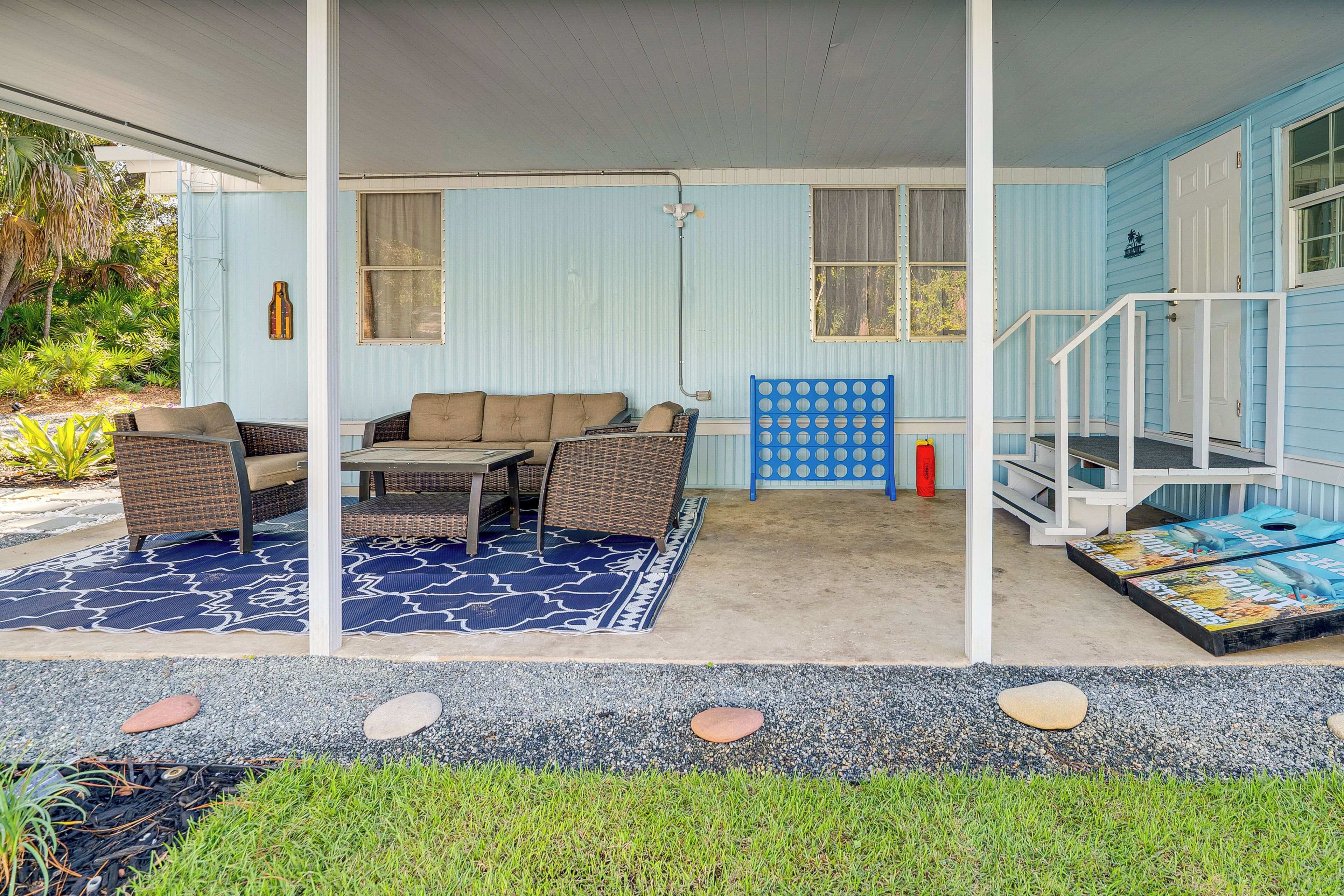 Een overdekt terras met een bank en stoelen, een tafel en een blauw tapijt met patroon.