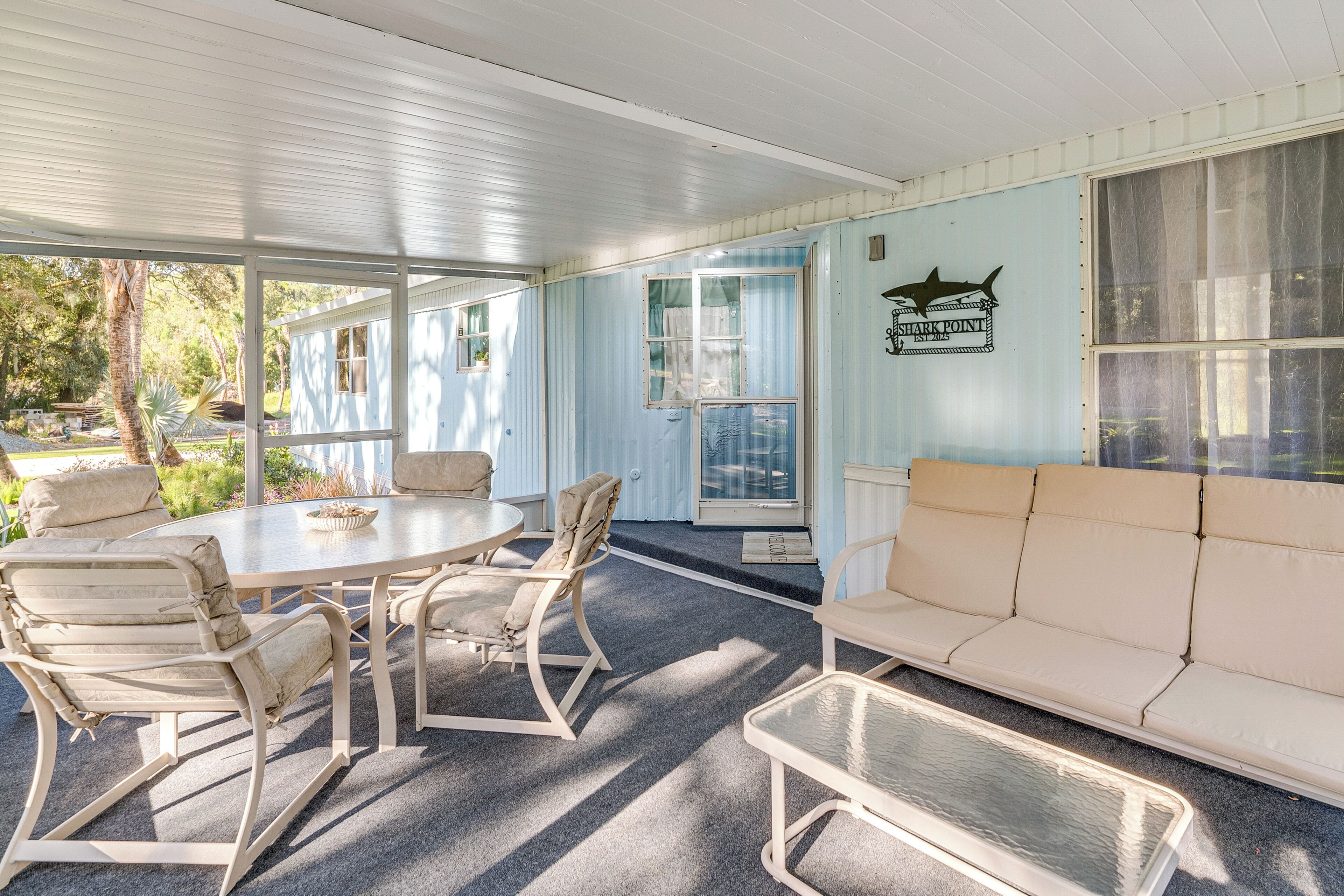 A covered outdoor seating area with a table and chairs, a sofa, and a sign reading "Shark Point."
